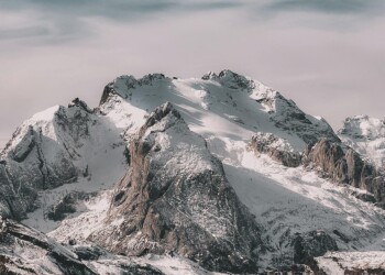 Snow-covered mountain range under cloudy sky Snowy mountain peaks with cloudy sky