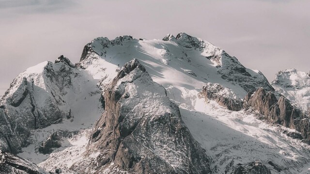 Snow-covered mountain range under cloudy sky Snowy mountain peaks with cloudy sky
